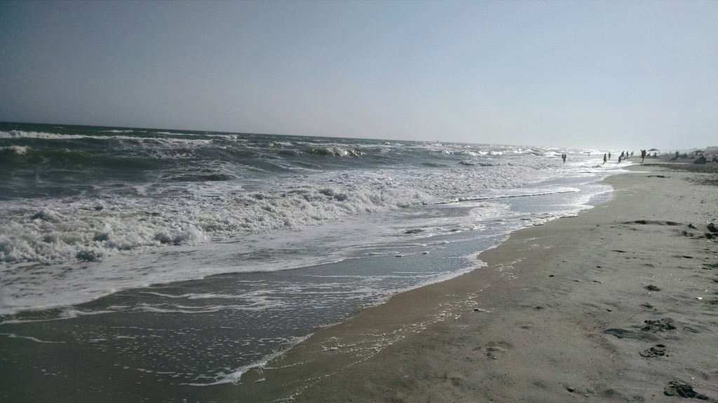 Waves gently crashing on a sandy beach under a clear sky.